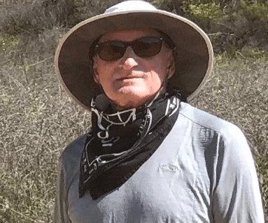 A man wearing sunglasses and a wide-brimmed hat stands outdoors