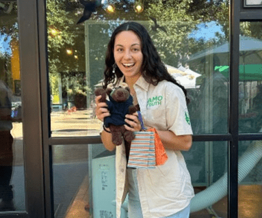 Young woman wearing a staff shirt smiles while holding a stuffed toy