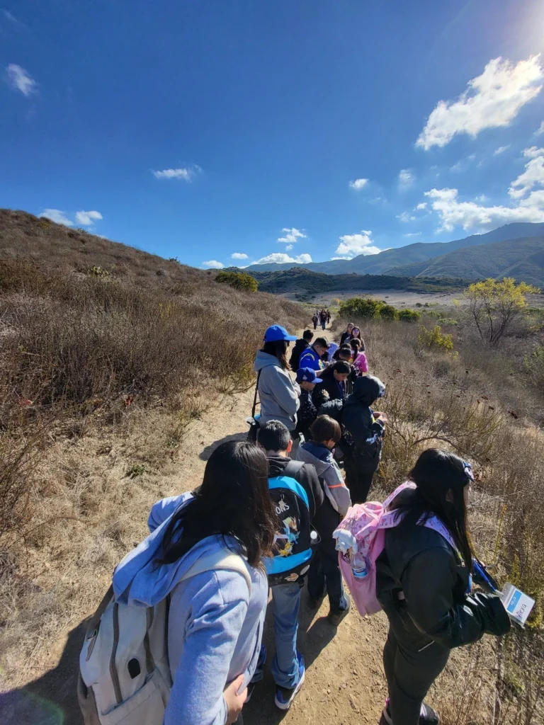 Students line up on a hiking trail, surrounded by hills and clear blue skies.