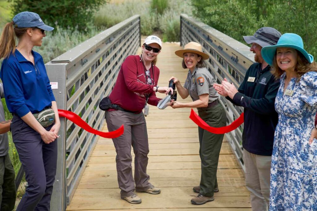 two smiling people cut a red ribbon to open a trail bridge
