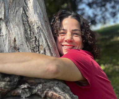 woman with short curly hair hugging a tree